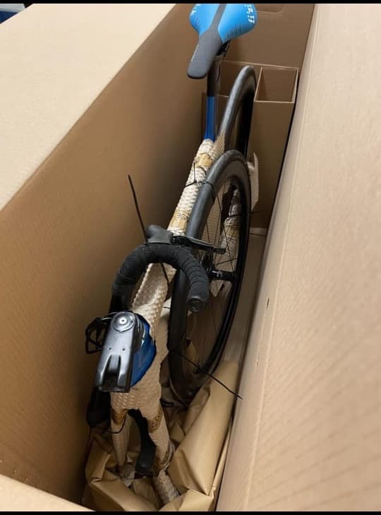 A road bicycle inside a corrugated crate, frame and forks wrapped in protective foam with the handlebars padded